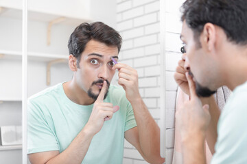 Handsome man grooming in front of the mirror in the bathroom. Young guy depilates with tweezers	