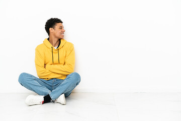 Young African American man sitting on the floor isolated on white background in lateral position