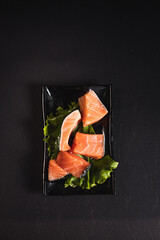 red fish on lettuce leaves on a black plate top view