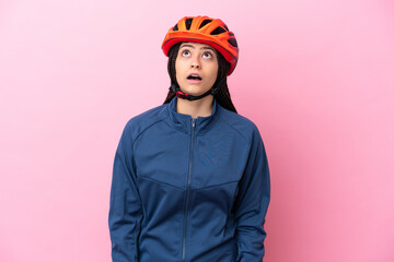 Teenager cyclist girl isolated on pink background looking up and with surprised expression - obrazy, fototapety, plakaty