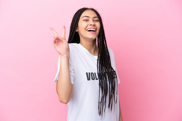 Teenager volunteer girl with braids isolated on pink background smiling and showing victory sign