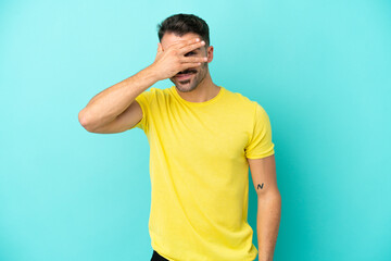 Young caucasian man isolated on blue background covering eyes by hands and smiling