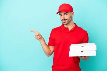 Delivery caucasian man picking up pizza boxes isolated on blue background pointing finger to the...