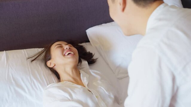 Asia people young adult man woman falling in love relax wake up smile laugh fun lying down at cozy home bed hotel enjoy hug kiss flirt date day. Joy happy asian lovers wife just married sweet newlywed