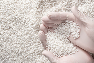 Close-up of a protectively gloved hand holding a lot of white plastic polymer granules.