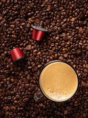 Top view of many roasted coffee beans and glass cup with fresh espresso coffee. Capsules for coffee machines.