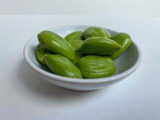 Parkia speciosa, the bitter bean, petai, or pete. Uncooked peeled seeds after peeled, in a bowl. Isolated on white background
