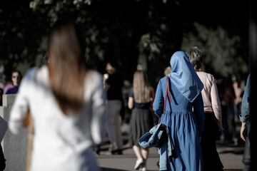 A Muslim woman wearing a blue headscarf and a blue dress walks down the street. View from the back without face