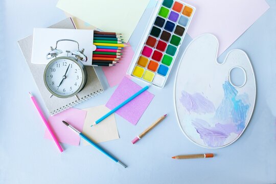 Flat lay composition with stationery, watercolor paints, brushes and colored pencils, palette,on a gray background. Back to school concept.
