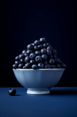 medium format shot of blueberries piled on top in a bowl on a dark blue surface, in the style of monochromatic minimalist portraits сreated with Generative Ai