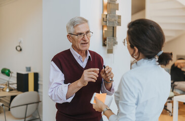 Experienced senior businessman in a conversation with a young female coworker. He gestures while holding a pen, in a bright modern office setting, signifying mentorship and collaboration.