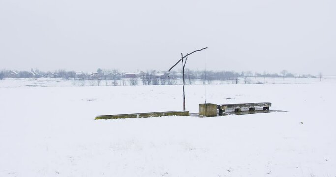 Old well pump made out of wood covered in snow in a field
