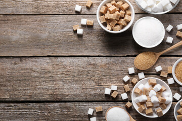 Different types of sugar in bowls and spoons on wooden table, flat lay. Space for text