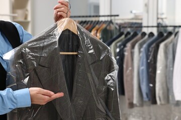 Dry-cleaning service. Woman holding jacket in plastic bag indoors, closeup and space for text