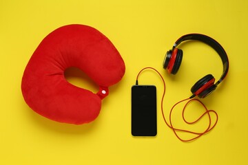 Red travel pillow, smartphone and headphones on yellow background, flat lay