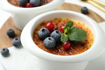 Delicious creme brulee with berries and mint in bowls on table, closeup