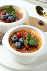 Delicious creme brulee with berries and mint in bowls on white table, closeup