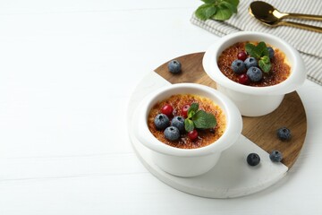 Delicious creme brulee with berries and mint in bowls on white wooden table. Space for text