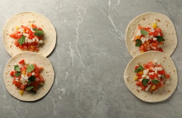 Delicious tacos with vegetables and parsley on grey marble table, top view. Space for text