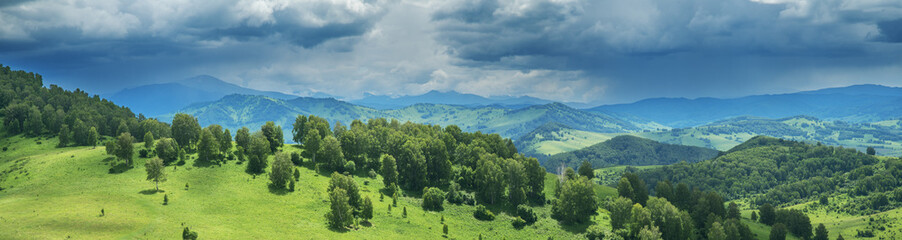 Mountains and hills in stormy weather, contrasting light, summer greenery of forests and meadows,...