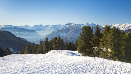 Snow-covered mountains with pine trees and blue sky in the backdrop, Tyrol, Austria