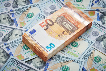 A neatly arranged stack of fifty-euro bills, standing out against a backdrop of scattered one-hundred-dollar notes. Intersection of international finance, juxtaposition and exchange global currencies.
