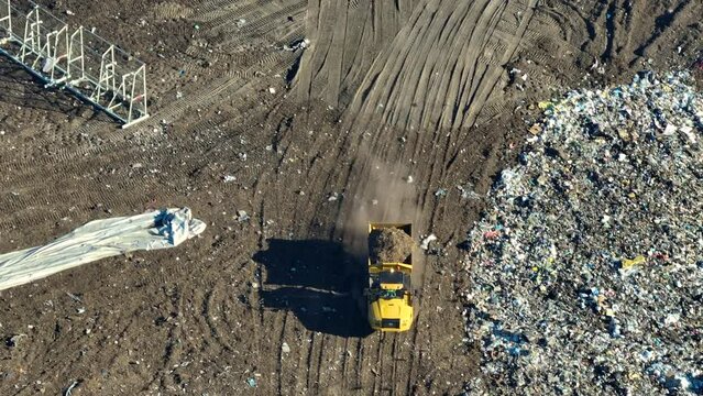 View from above of landfill dump site for garbage waste management. Bulldozer tractors burying large amount of trash under the ground. Harmful impact of modern consumerism on environment