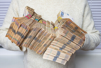 Money depreciation and inflation, symbolic image. Bundles of Ukrainian hryvnia. Female holding a many stacks of banknotes.