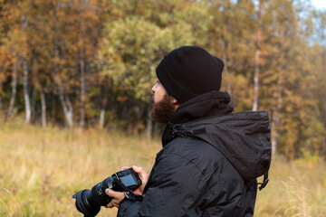hombre con barba y ropa de invierno negra con cámara fotografica en mano