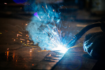 Master is doing welding at his workplace in the workshop, while sparks are flying all around, they...