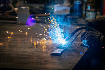 Master is doing welding at his workplace in the workshop, while sparks are flying all around, they are wearing a protective helmet.
