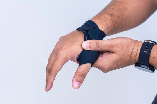 A man massages the first metacarpal joint. Wearing an ultra-thin compression wrist and thumb brace for texting thumb syndrome, carpal tunnel or tendonitis.