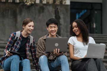Diversity, college student focusing on laptop work or reading while other classmates in the background, outdoor portrait on campus campus.