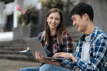 Diversity, college student focusing on laptop work or reading while other classmates in the background, outdoor portrait on campus campus.