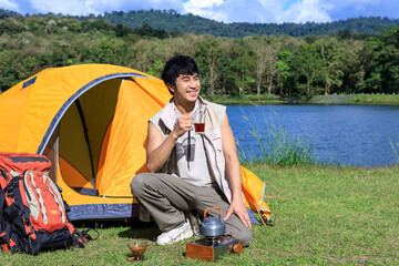 Asian male man drinking coffee and feeling relax with camping tent beside lake and mountain