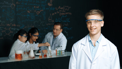 Smart student looking at camera while diverse group doing experiment. Attractive academic boy...