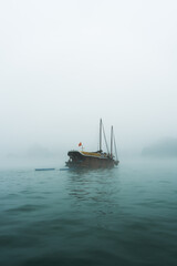 A solitary boat emerges from the mist on a serene water surface.