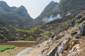 Terraced fields nestled in a mountainous landscape, with a hint of smoke rising in the distance