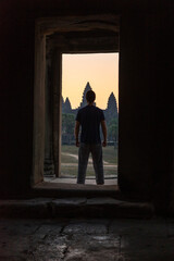 Silhouette of a person standing in a doorway with ancient temples in the background at dusk.