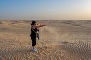 Fototapeta na wymiar Side view of young woman, female tourist releasing sand from hands in sahara desert, Tunisia. 