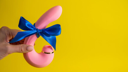 Woman holding curved pink vibrator with blue ribbon on yellow background. Copy space. 