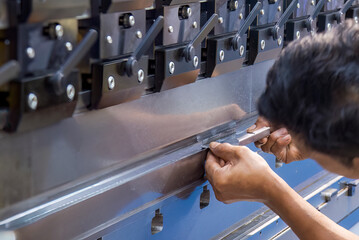 Close up the bending machine operator hold the sheet metal parts with rubber glove.