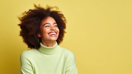 Happy optimistic African American woman in colorful pastel green clothes laughing isolated on yellow background.