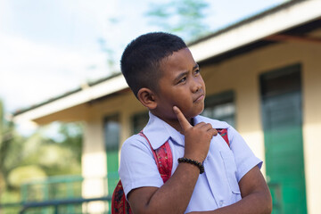 A young boy with a backpack contemplating while standing outside his classroom, showcasing school life.