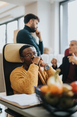 Pensive African American man in a yellow sweater listens intently at a casual office meeting, with...
