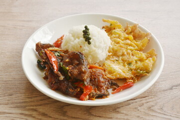 spicy stir fried crispy catfish curry with basil leaf on rice and Thai egg omelet on plate