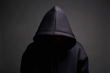 Man in Black Hood posing in dark studio. Boy in a hooded sweatshirt - obrazy, fototapety, plakaty
