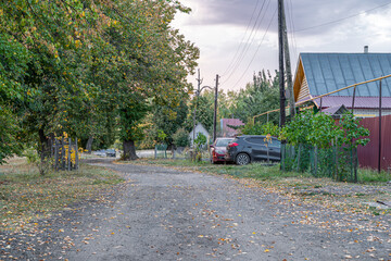 Rural setting with rustic dirt road along private homes with cars among green bush trees on a warm fall afternoon. Clean air green grass and lime oak trees for health, quiet privacy with nature.