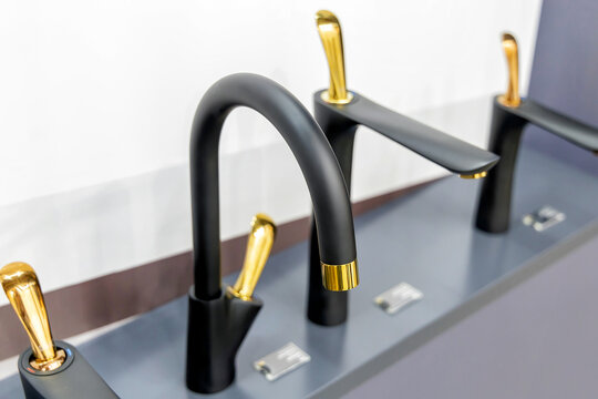 Black sink taps with gold handles are set on a dark countertop. Modern taps with elegant design and contrasting color combinations. Plumbing store, showroom or fair