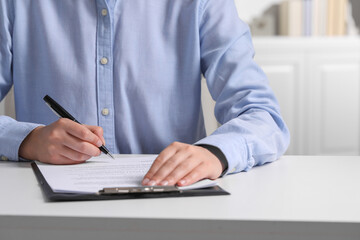 Woman signing document at white table indoors, closeup. Space for text